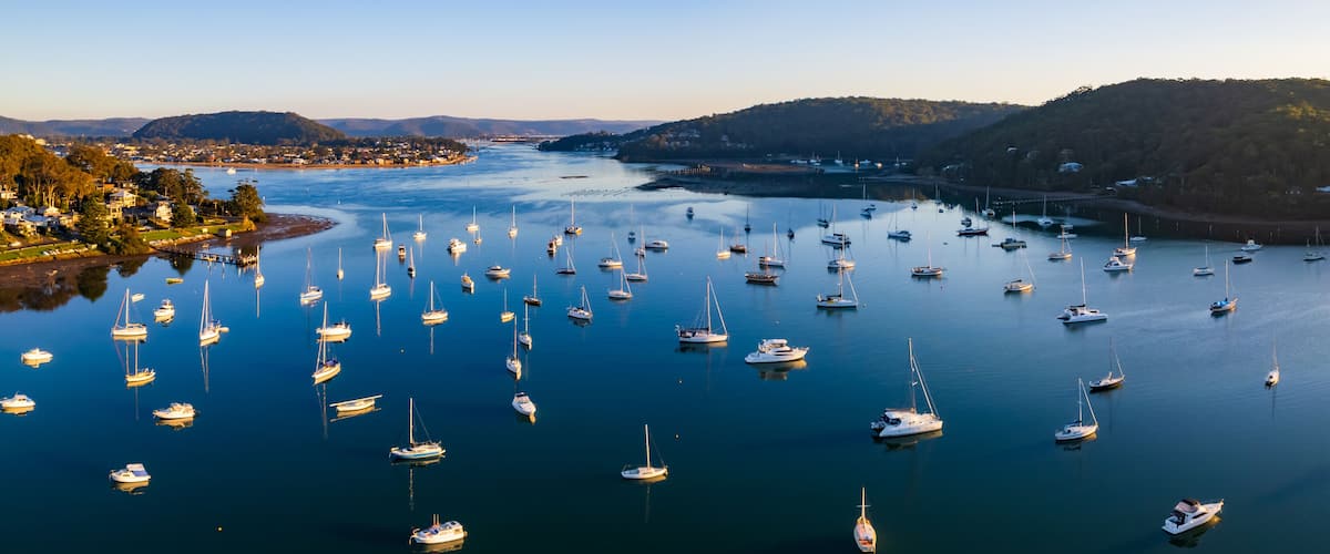 A harbor filled with numerous sailboats and yachts, surrounded by hills and a small town.