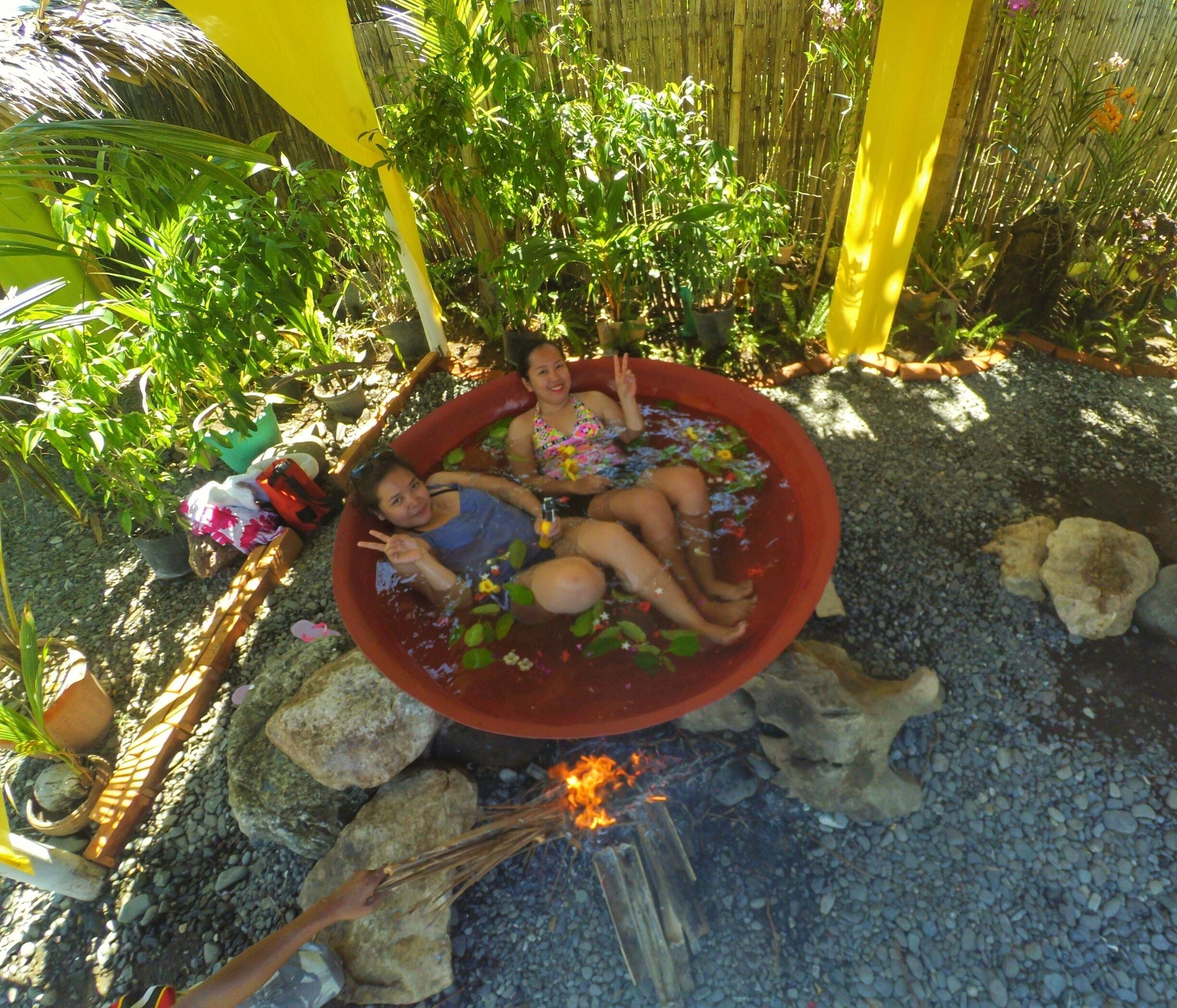 A hot tub filled with water and flowers, surrounded by rocks and plants.