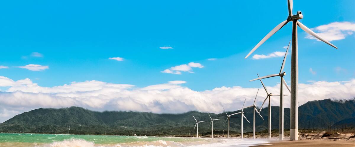 A beach with wind turbines and mountains in the background.