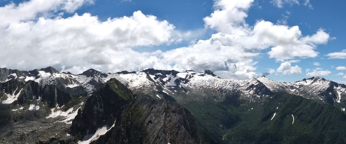 A mountain range with snow-capped peaks and a partly cloudy sky.
