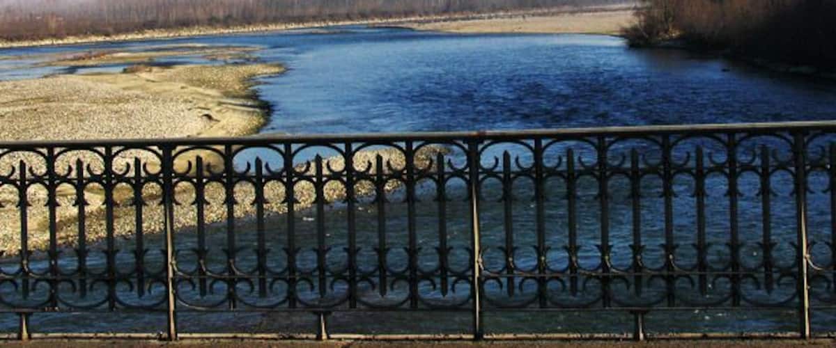 A river with a metal fence in the foreground and trees in the background.