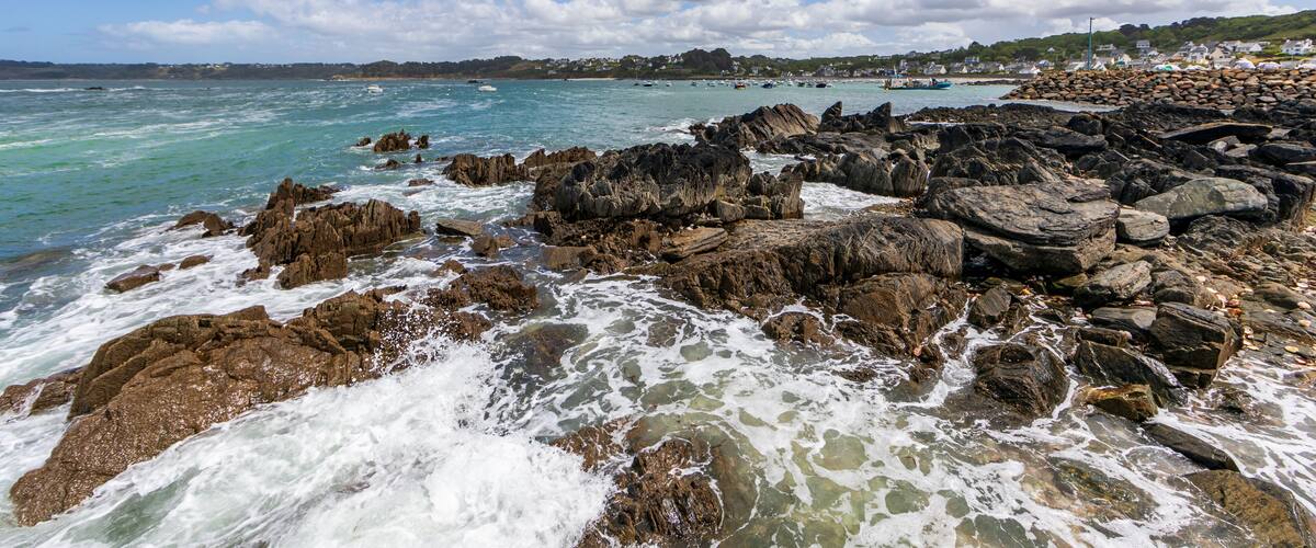 A rocky coastline with waves crashing against the rocks under a partly cloudy sky.