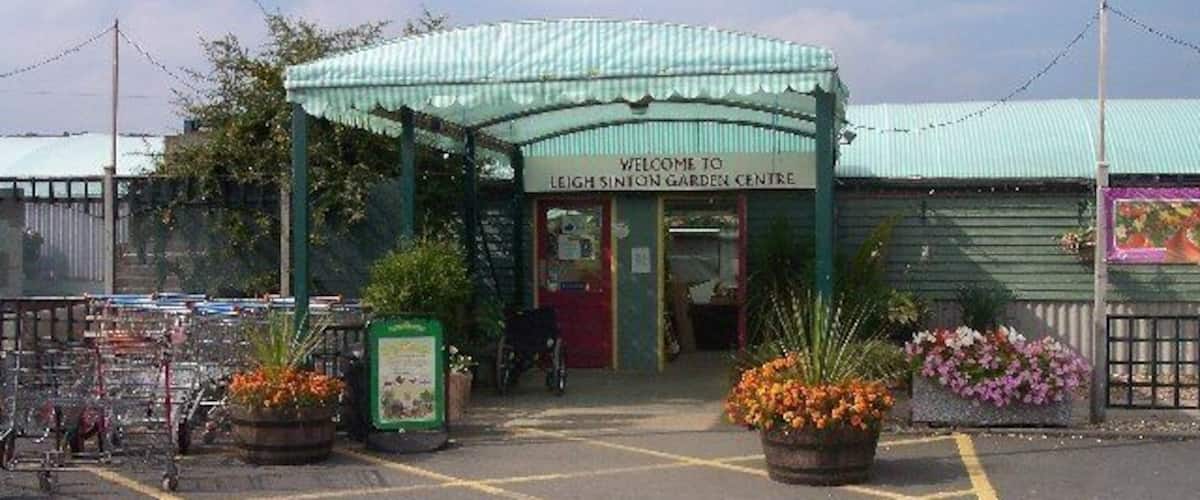 A garden center entrance with a green canopy, flower pots, and a sign welcoming visitors.