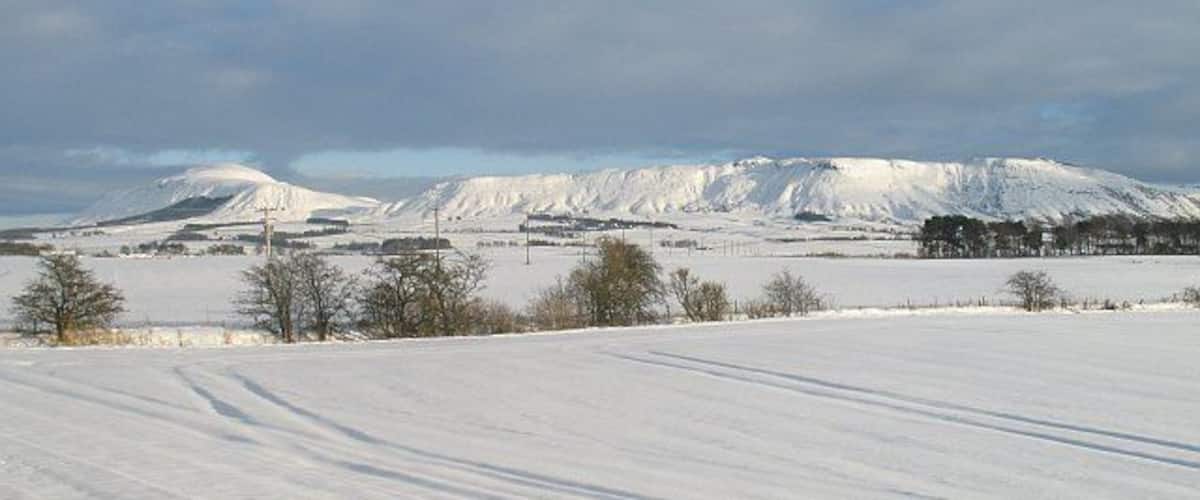 A snow-covered landscape with a mountain in the background and a clear sky.