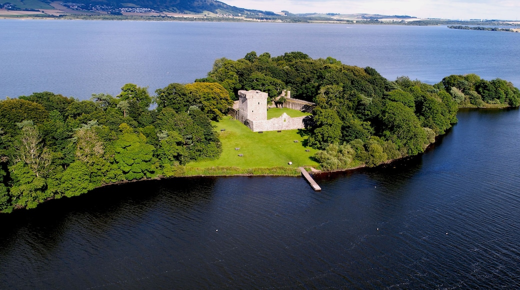An aerial view of a small island with a castle surrounded by dense greenery and a calm body of water.