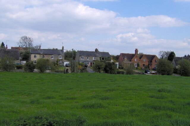 A rural landscape with houses, a green field, and a partly cloudy sky.