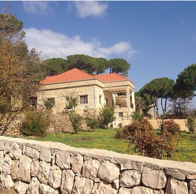 Traditional old Lebanese house  made of white stones with red brick roof surrounding by pine tees .