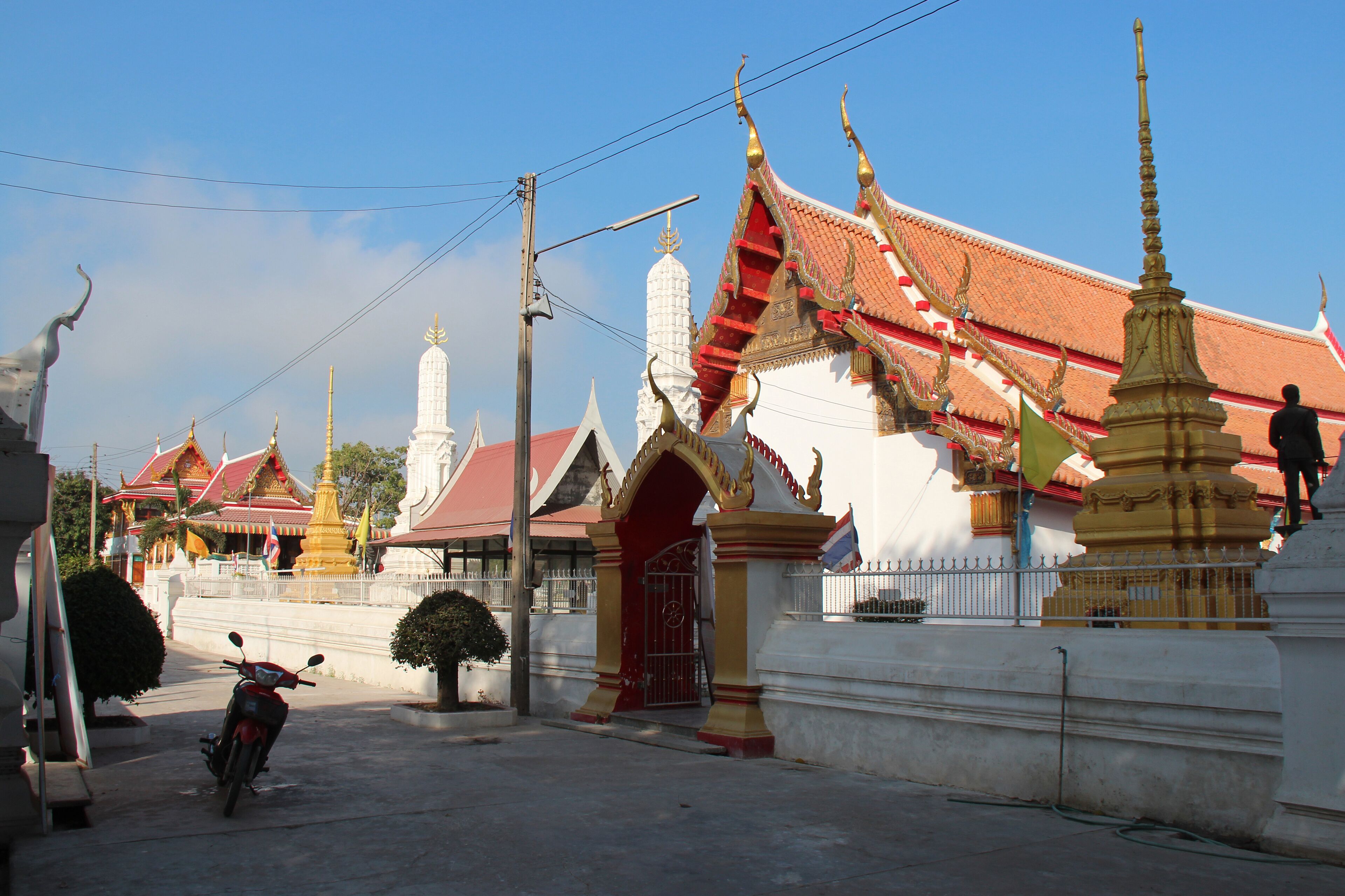 A traditional Thai temple with ornate architecture, a red and gold roof, and a golden stupa.