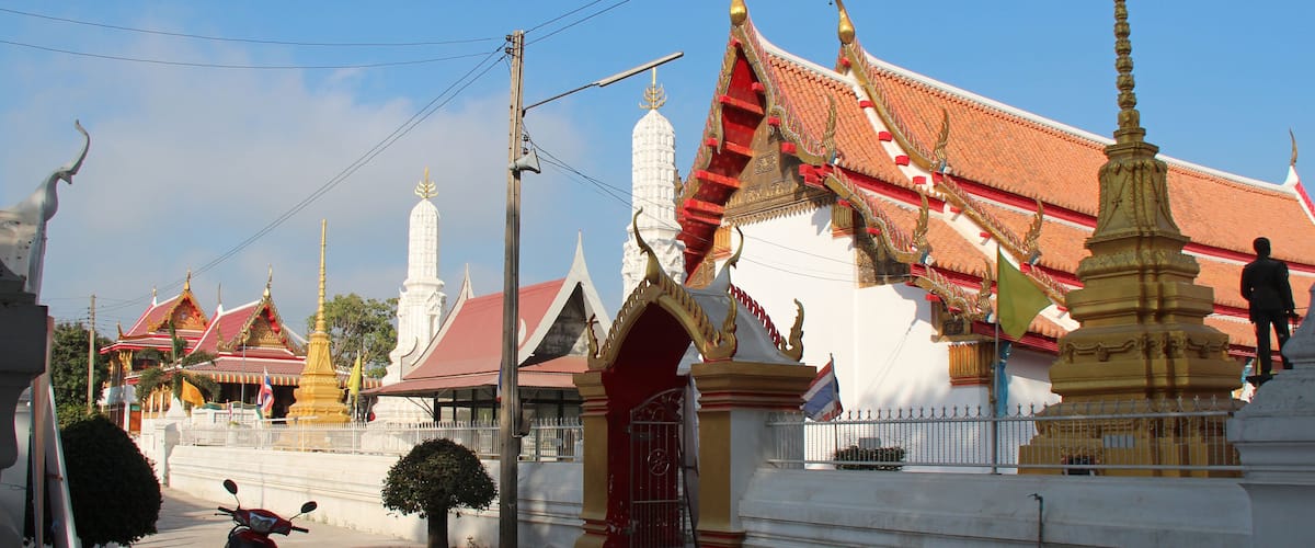 A traditional Thai temple with ornate architecture, a red and gold roof, and a golden stupa.