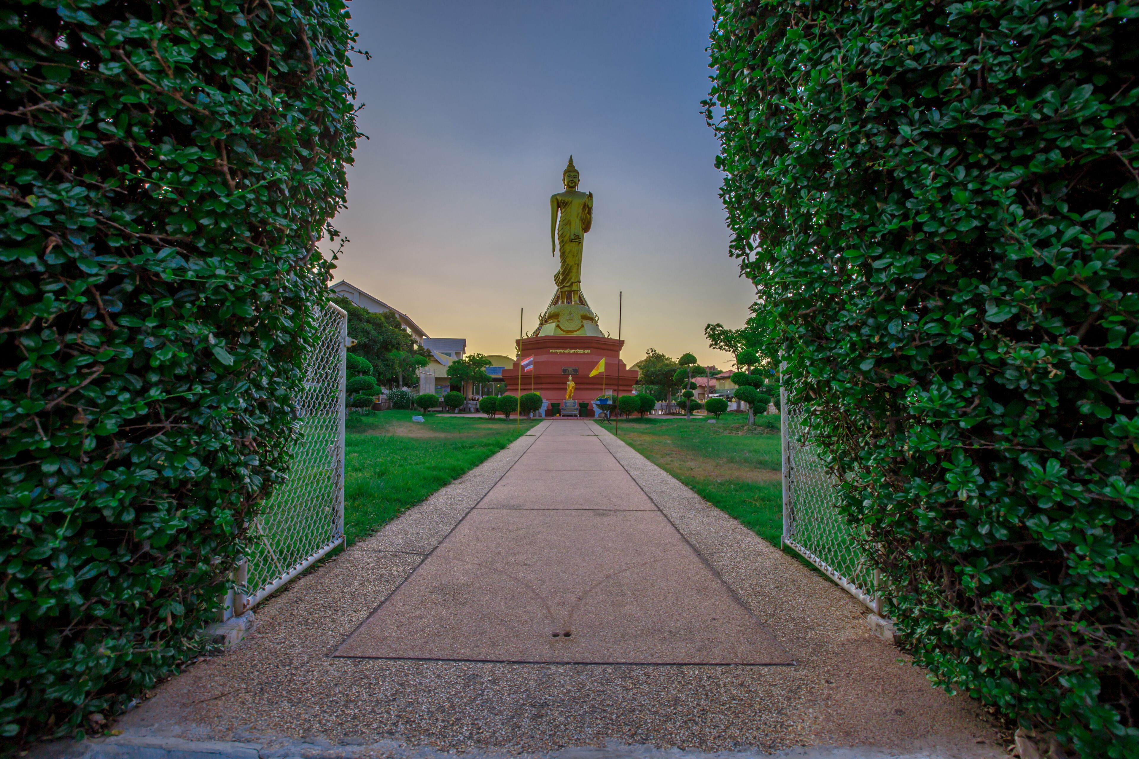 A golden statue in a park with a pathway leading to it, surrounded by greenery.