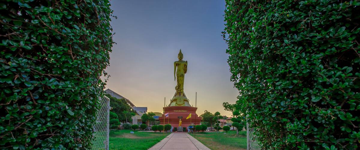 A golden statue in a park with a pathway leading to it, surrounded by greenery.