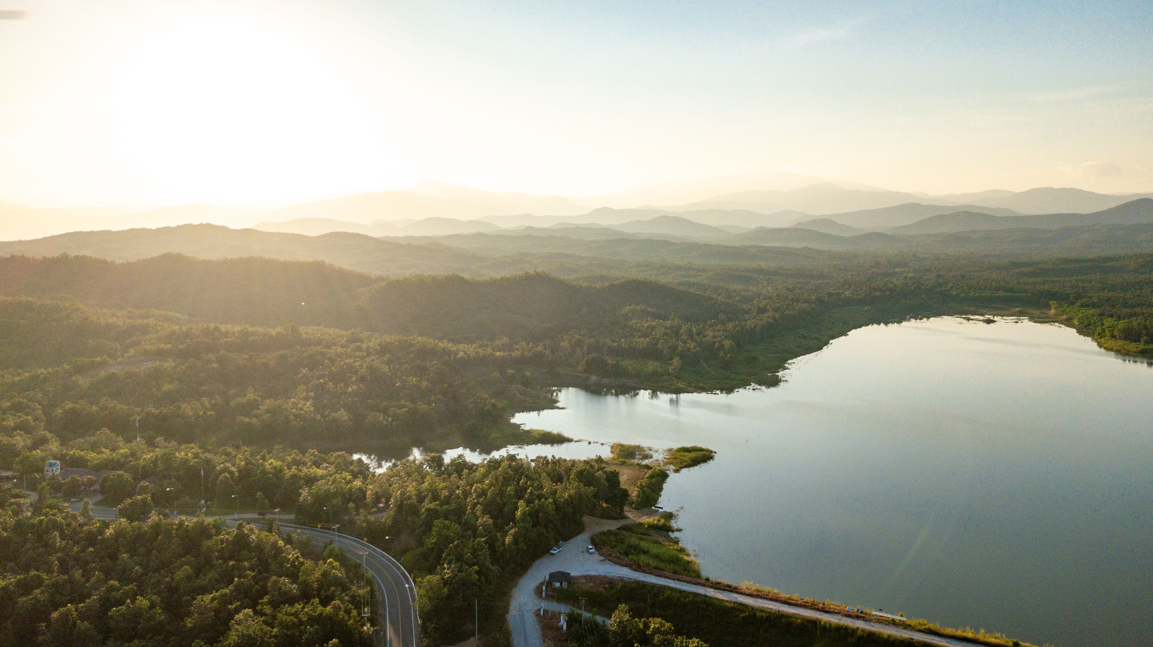 A lake surrounded by forested hills, a winding road, and distant mountains.