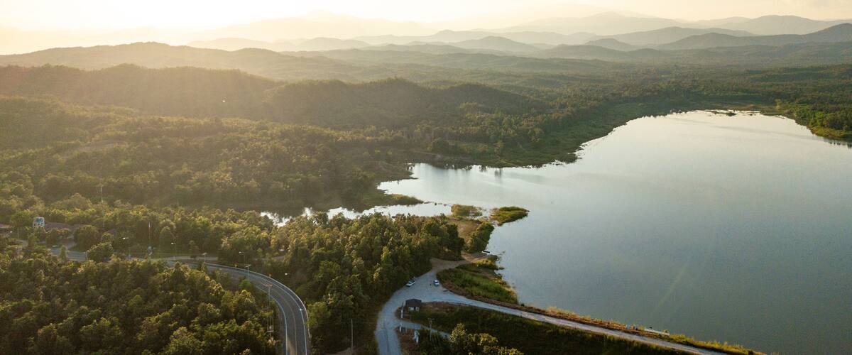 A lake surrounded by forested hills, a winding road, and distant mountains.