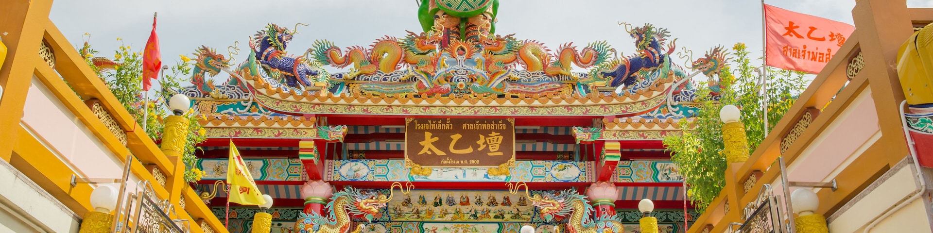 Entrada de un templo con una gran estatua, decoraciones coloridas y un letrero en idioma extranjero.