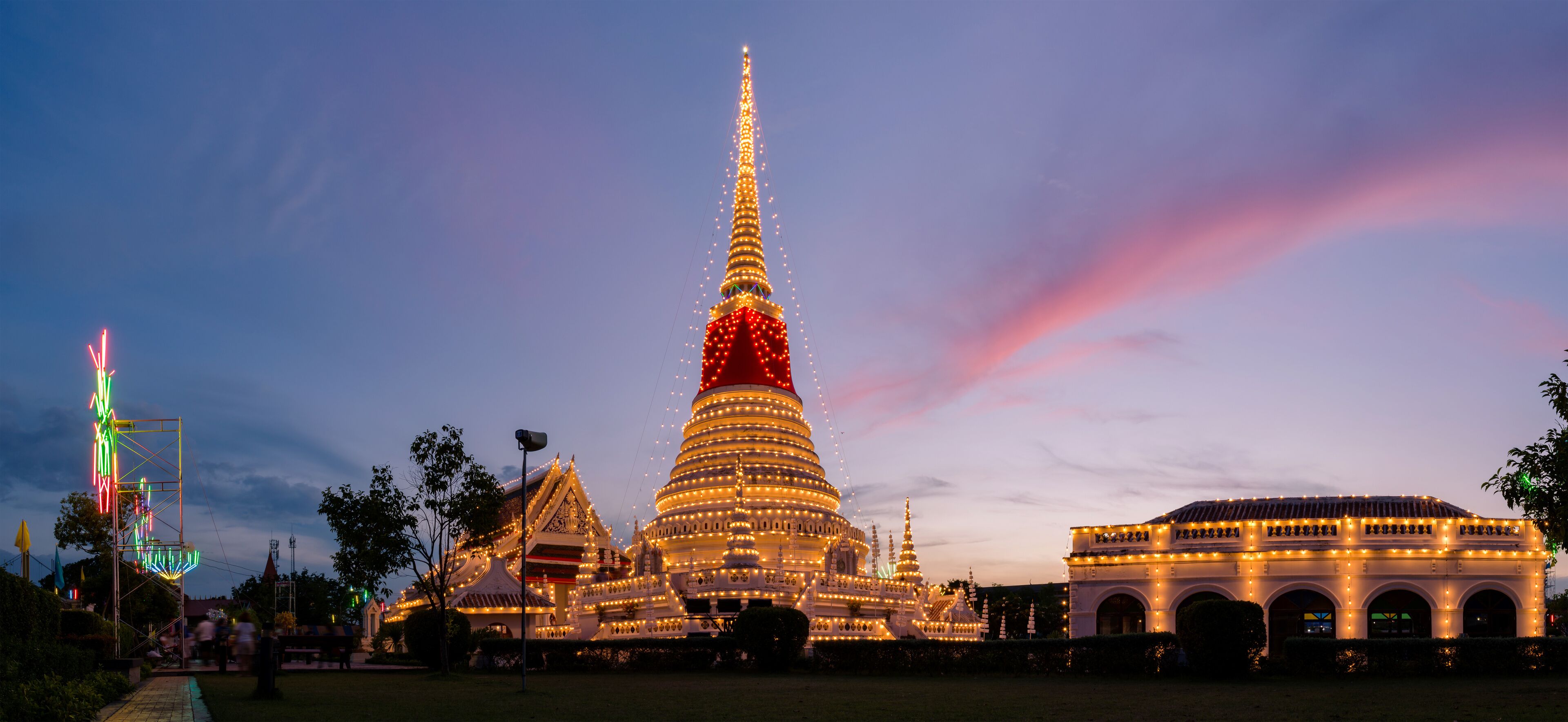 A brightly lit temple complex at dusk with a prominent spire and surrounding structures.