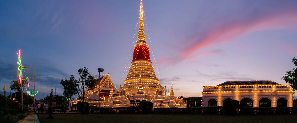 A brightly lit temple complex at dusk with a prominent spire and surrounding structures.