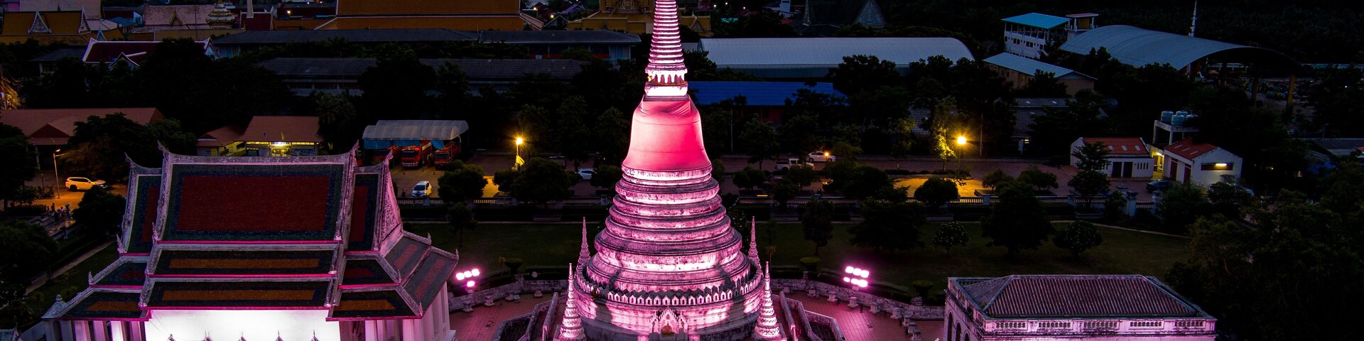 Un templo grande de varios niveles con una aguja, rodeado de edificios más pequeños y un paisaje urbano de fondo.