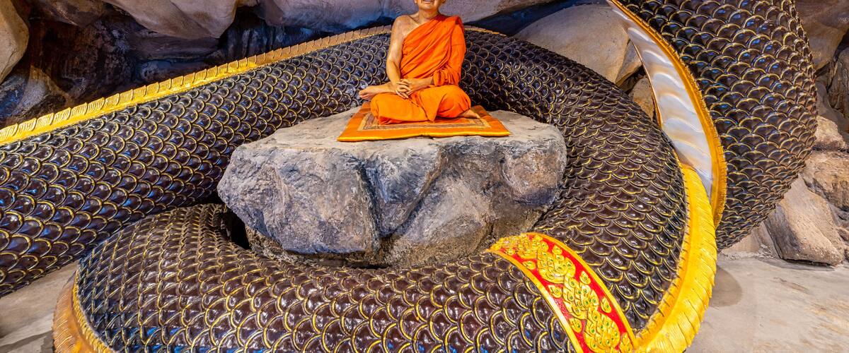 A statue of a monk meditating on a rock amidst a large, ornate snake sculpture.