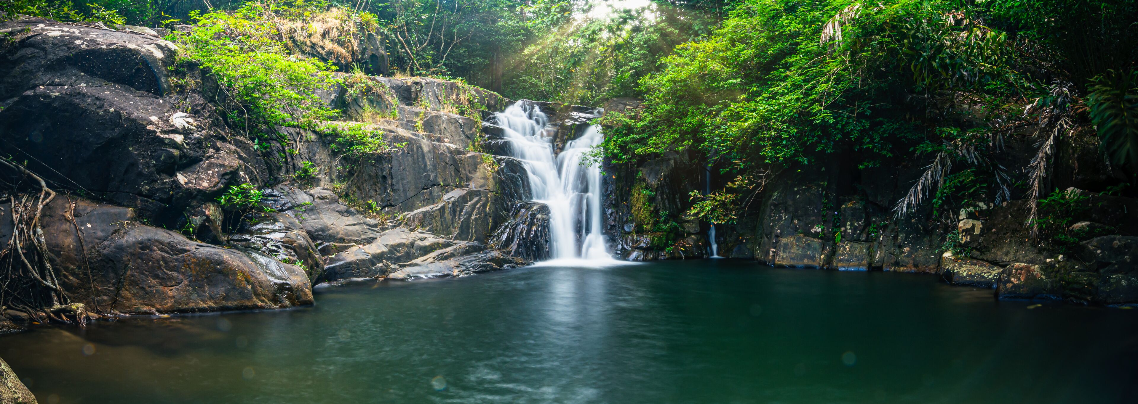A waterfall cascading into a clear pool surrounded by rocky terrain and lush greenery.