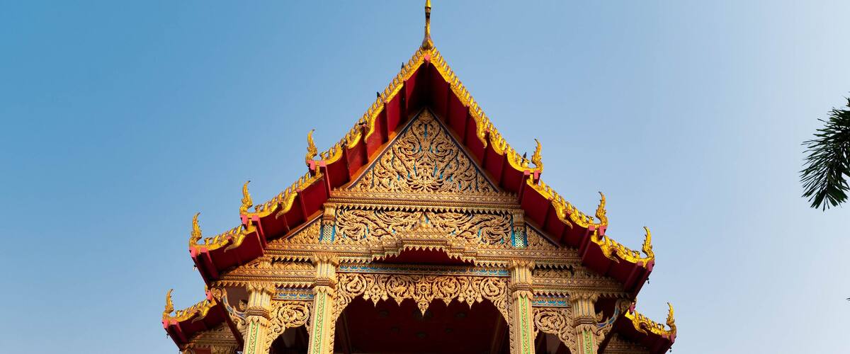 A temple with ornate golden decorations and a red roof, surrounded by stone steps and a metal railing.