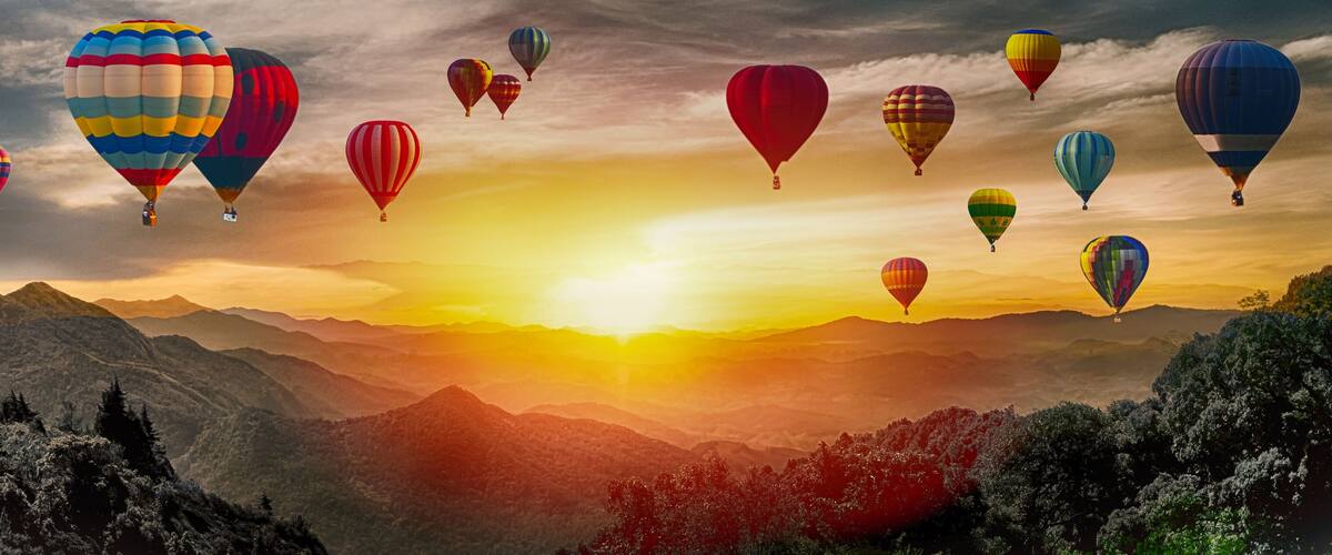 A landscape with mountains and hot air balloons at sunset.