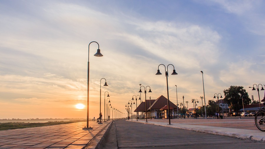 Ein Sonnenuntergang über einer Uferpromenade mit Straßenlaternen und einem kleinen Pavillon.