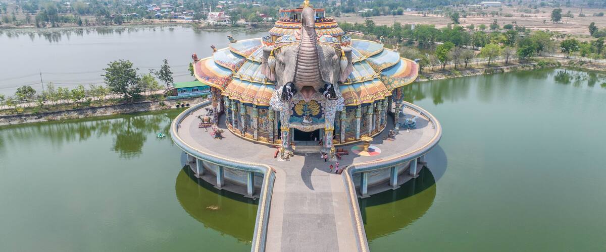 A large, ornate temple with a golden statue on top, surrounded by water and greenery.