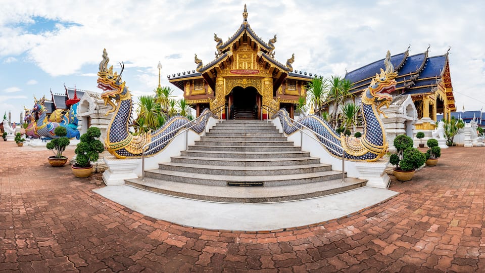 A temple with ornate golden roofs and blue and gold decorations, surrounded by potted plants and a paved walkway.