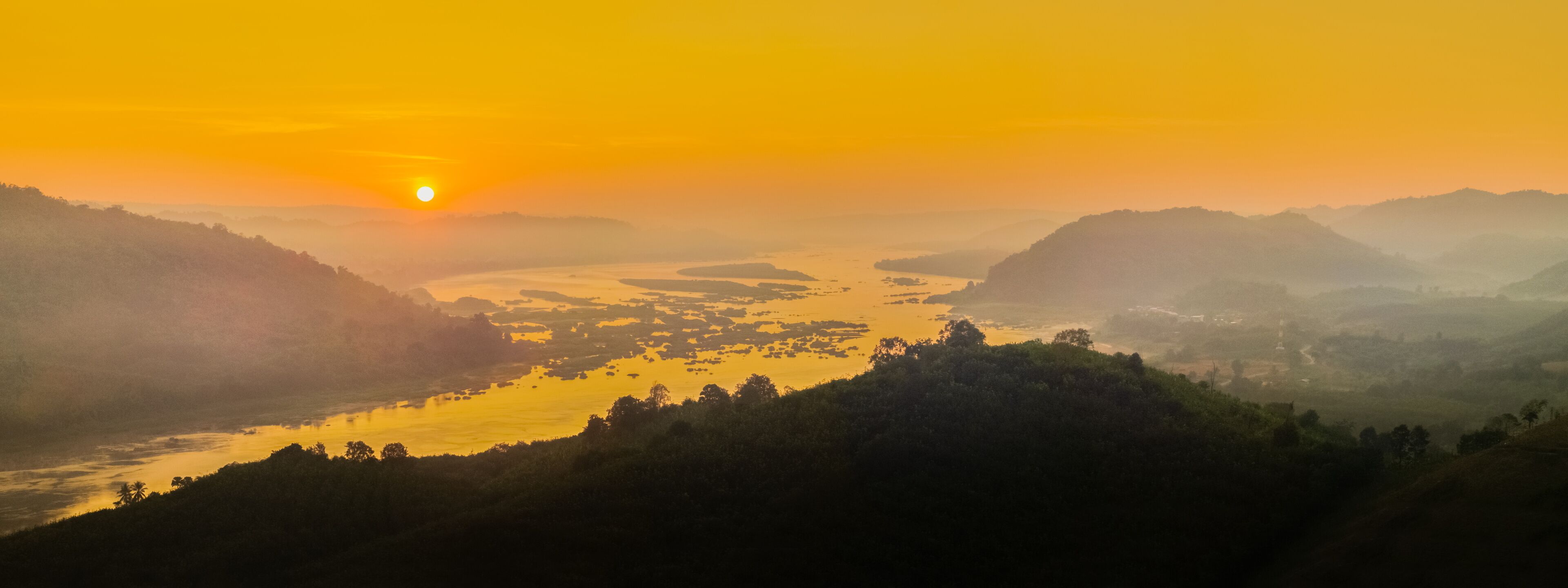 A sunrise over a river valley with hills on either side.