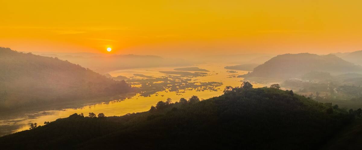 A sunrise over a river valley with hills on either side.
