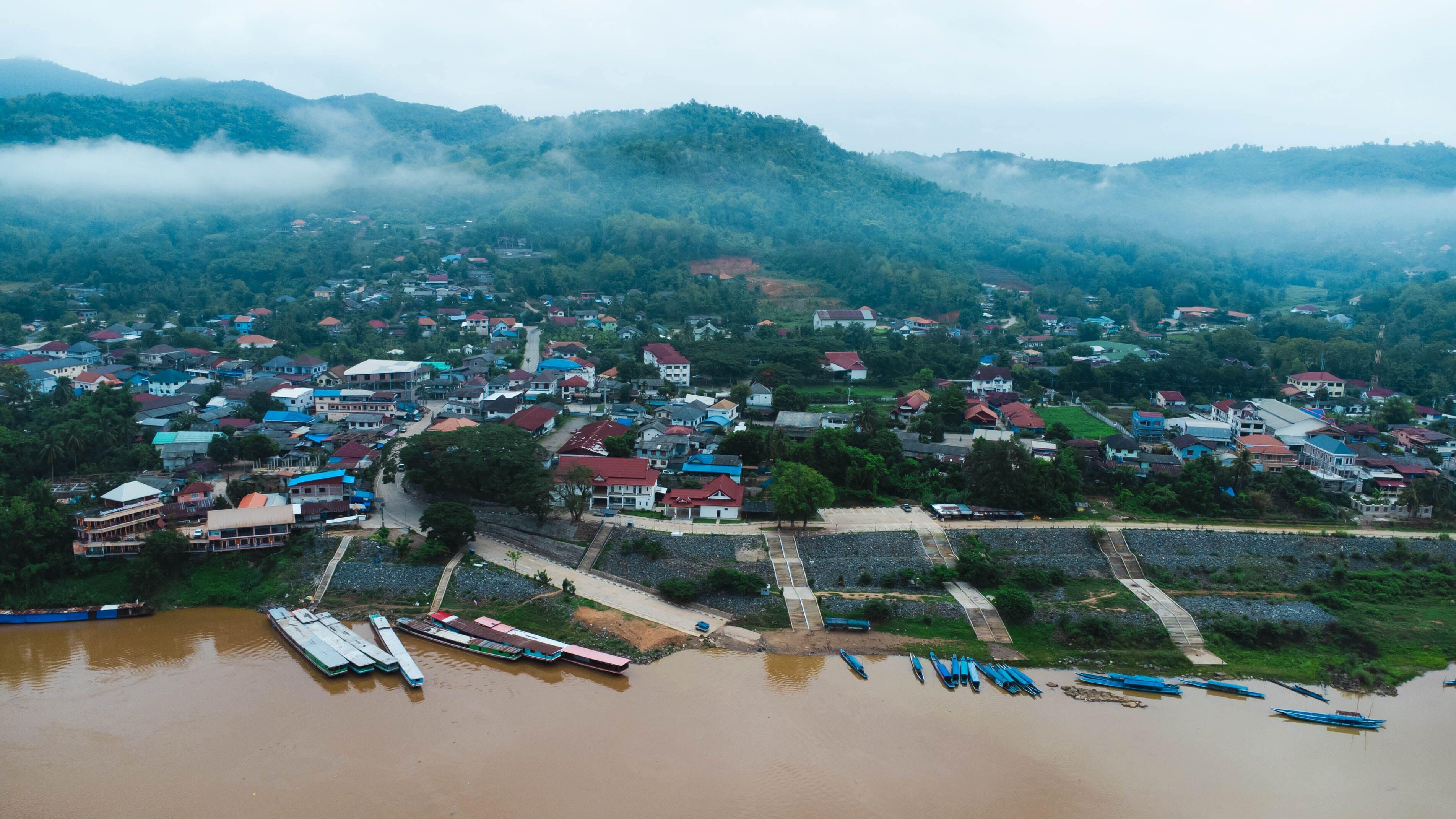 Aerial view of the mighty Mekong River winding from Chiang Khong, showing the vastness and beauty of the muddy waterway contrasting with the surrounding lush mountains and Laos villages.