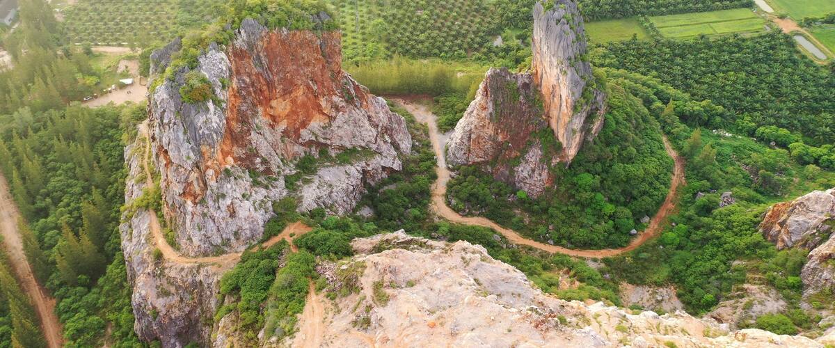 A mountainous landscape with two prominent rock formations surrounded by dense forests and agricultural fields.