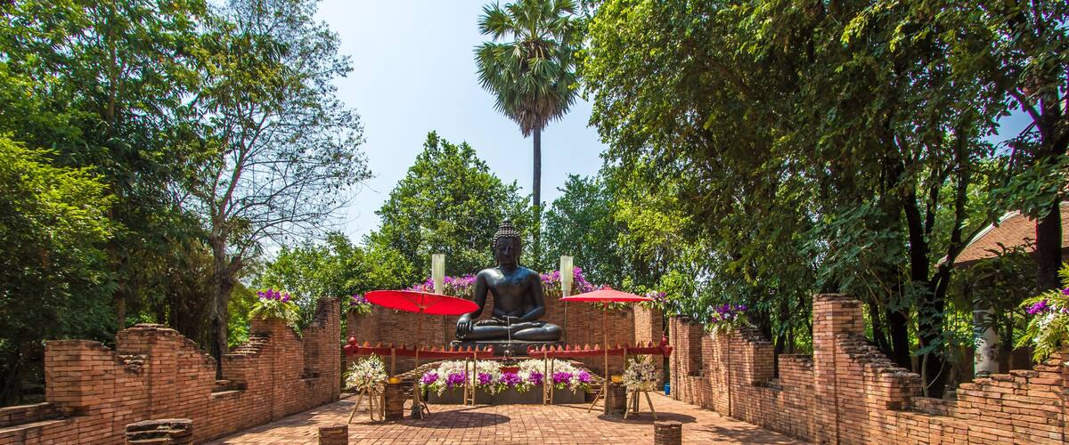 A Buddha statue in a garden with brick pathways and red umbrellas.