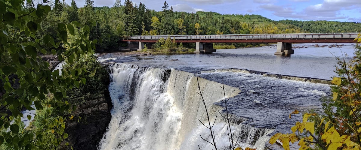 A waterfall, a bridge, and surrounding forest.