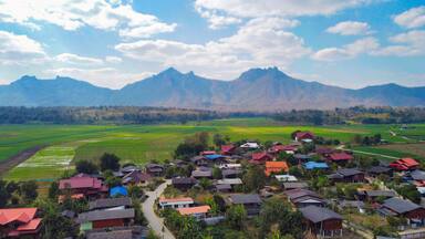 A village with colorful houses and green fields, surrounded by mountains.