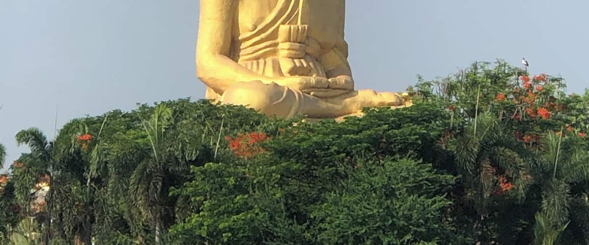 A large golden statue of a seated figure with a serene expression, surrounded by lush greenery and red flowers.