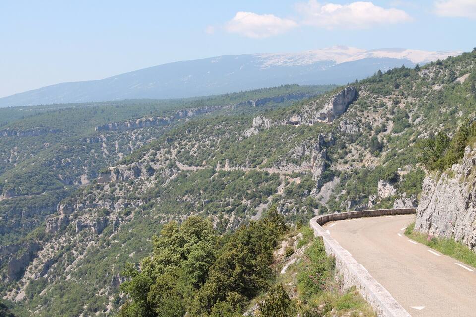 A winding mountain road with rocky cliffs and dense greenery.