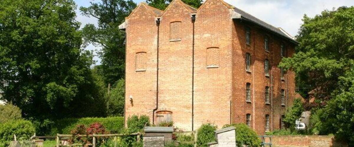 A large brick building with multiple windows and a grassy area in front.