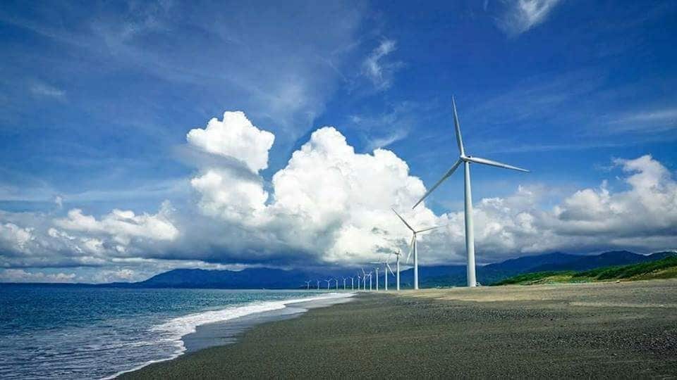 A beach with wind turbines and a cloudy sky.