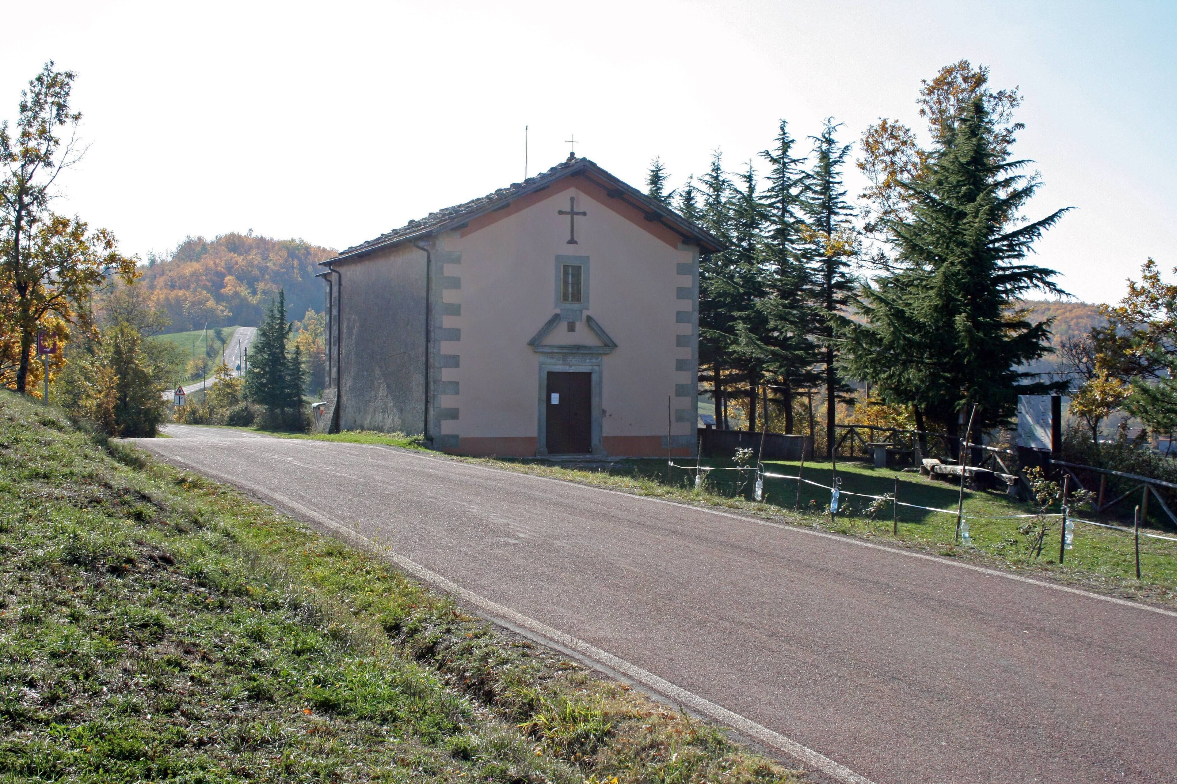 A small church with a cross on the roof, surrounded by trees and a road.