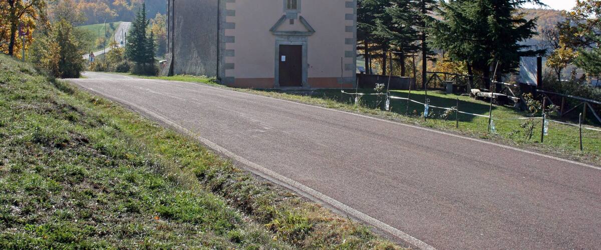 A small church with a cross on the roof, surrounded by trees and a road.