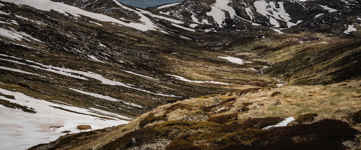 A mountainous landscape with snow patches and a valley.