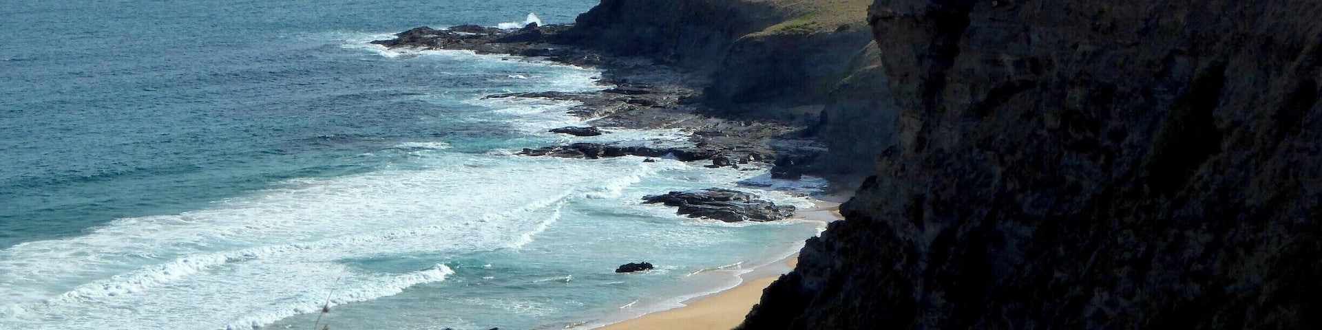 A coastal landscape with a sandy beach, rocky cliffs, and grassy hills.