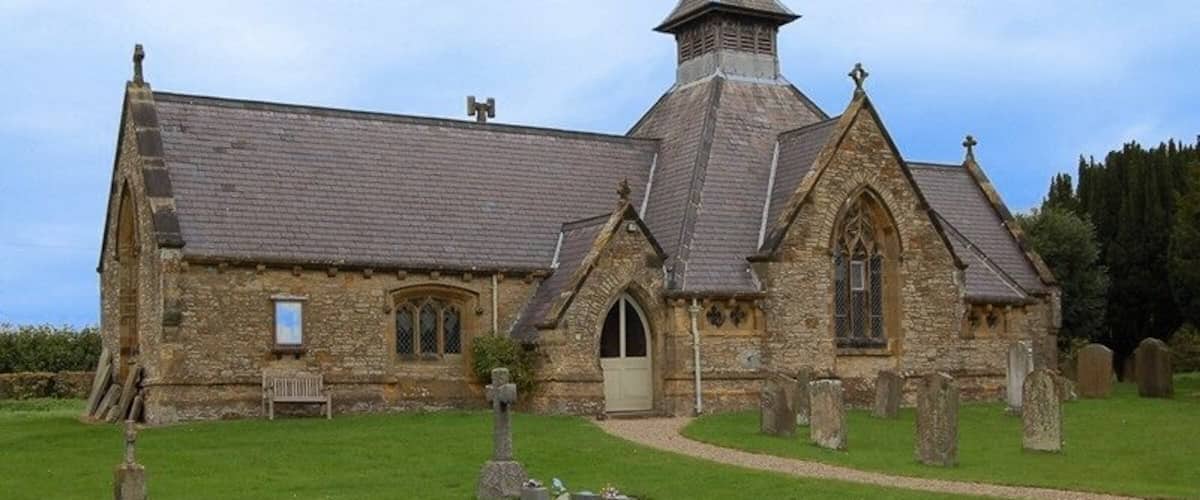A stone church with a pointed steeple, surrounded by a cemetery with headstones.