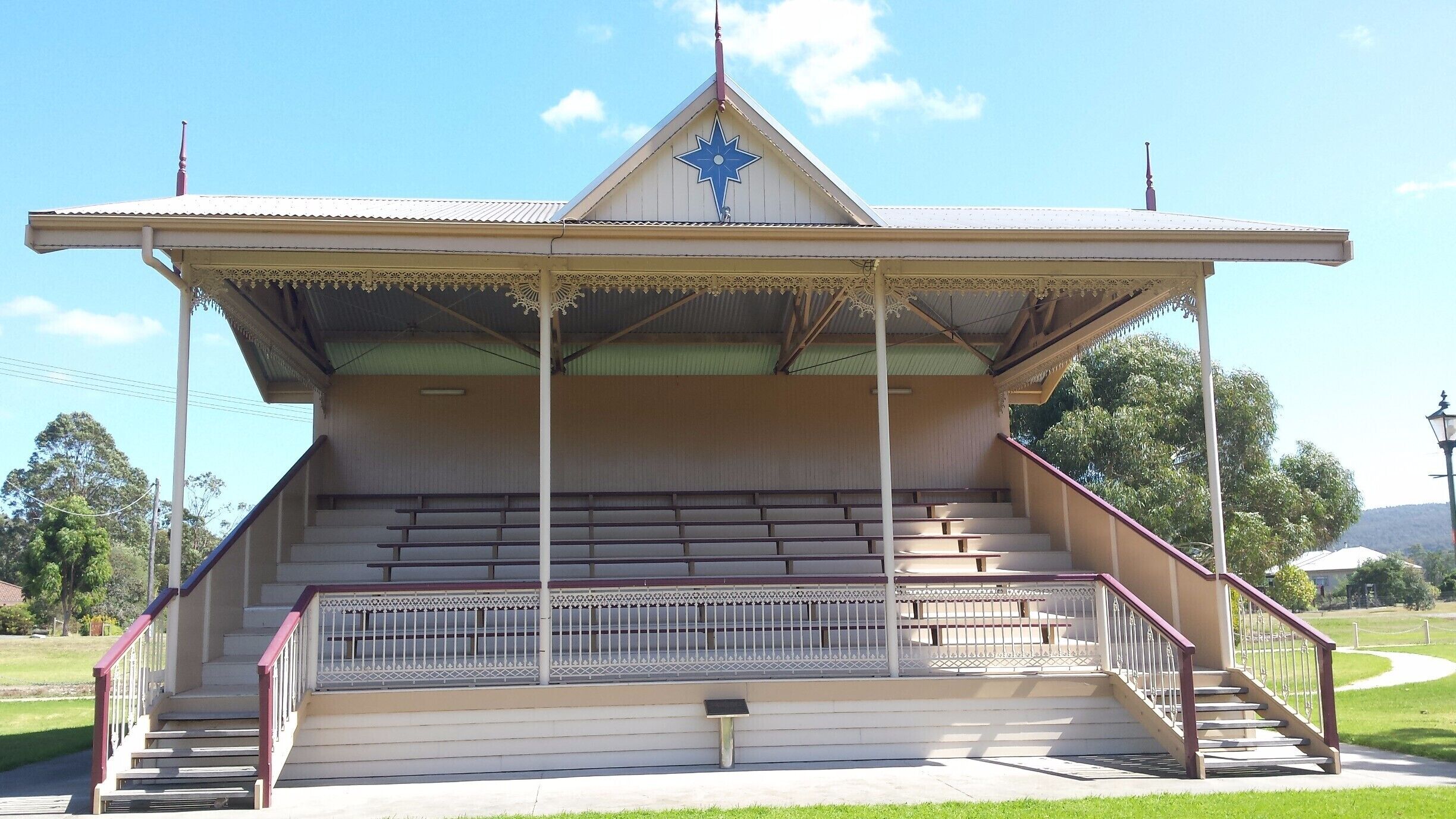 A gazebo with a star-shaped roof, a staircase leading up to it, and a grassy area in the background.