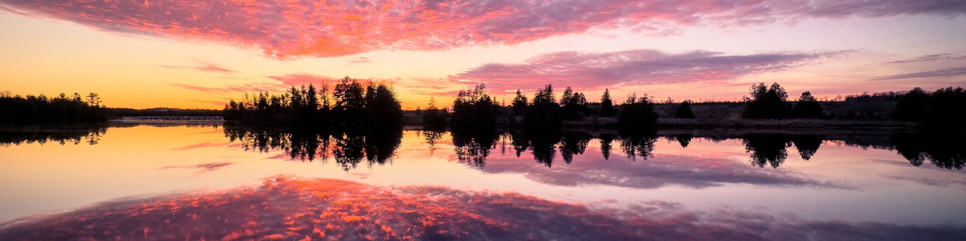 A sunset over a calm lake with trees silhouetted against the sky.