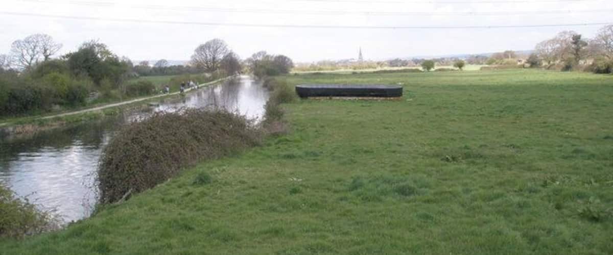 A canal with a grassy bank and a bridge in the distance.