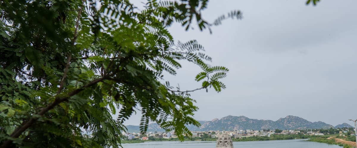 A temple with a water body in the foreground, surrounded by greenery and mountains in the background.