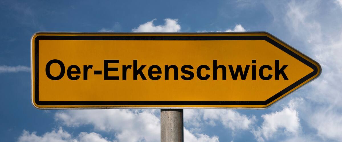 A directional sign with the text "Oer-Erkenschwick" against a blue sky with clouds.
