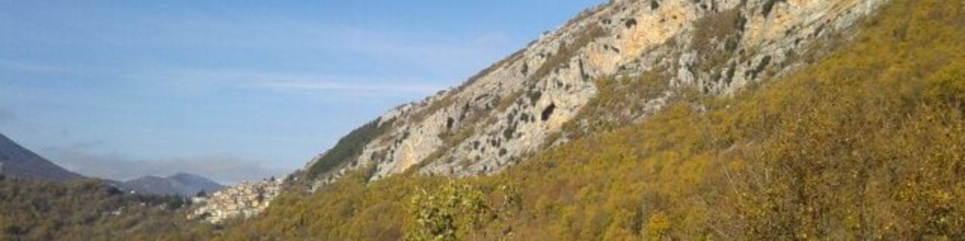 A mountainous landscape with autumn foliage, rocky cliffs, and a clear sky.